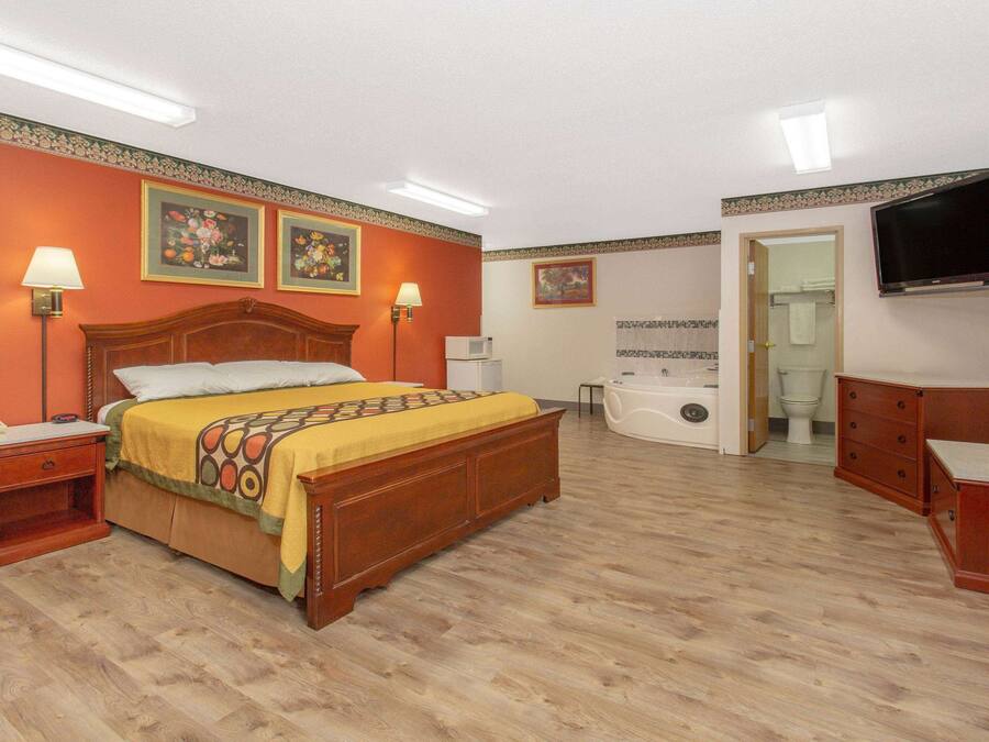 A hotel room with a wooden bed, a nightstand, a desk, a chair, a television, a bathroom with a bathtub, and a toilet.