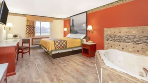 A hotel room with a bed, a desk, a chair, a TV, a window with curtains, a wall-mounted lamp, and a bathtub. - Super 8 by Wyndham Bedford (Bedford)