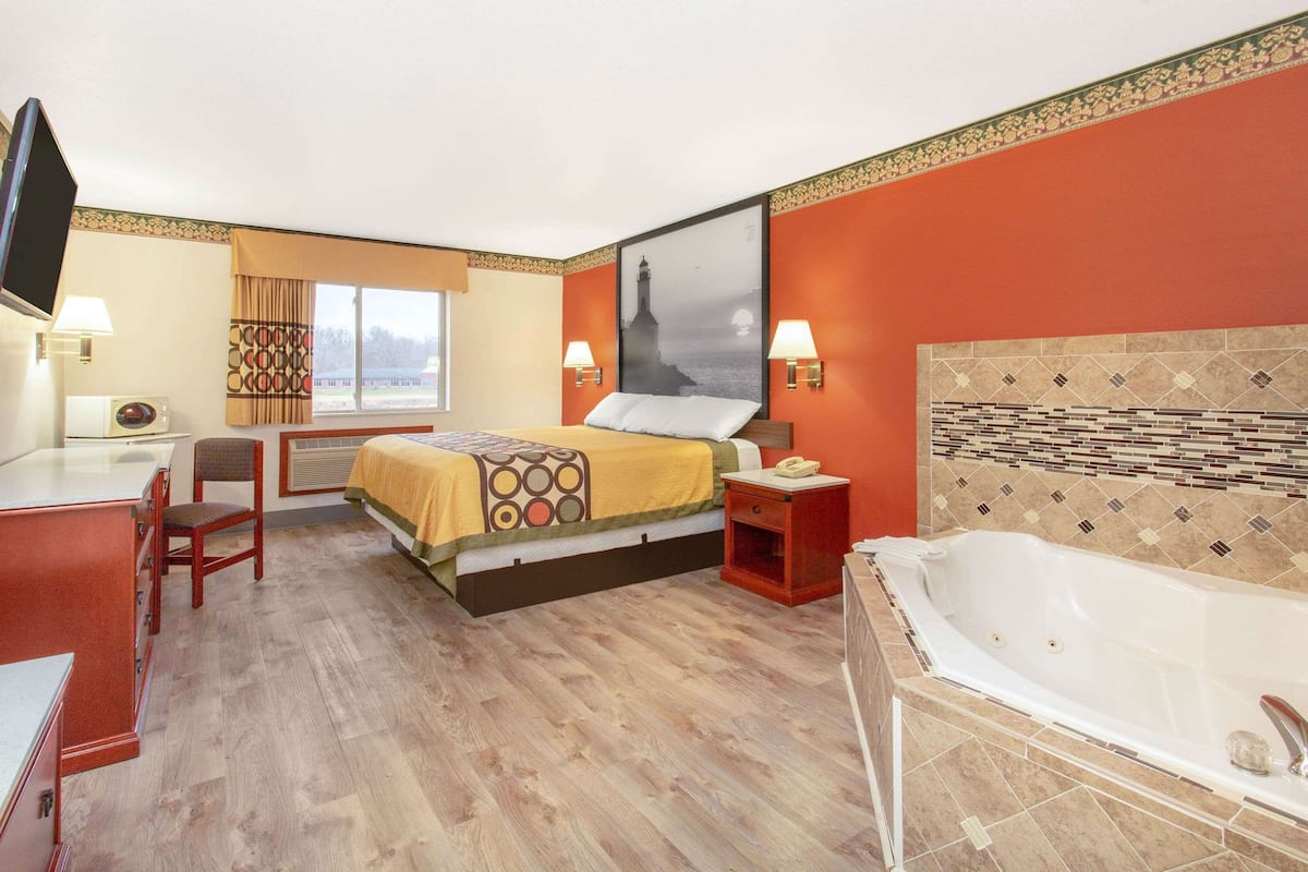 Hotelkamer met een bed, bureau, stoel, televisie, raam met gordijnen, wandlamp en een bad.