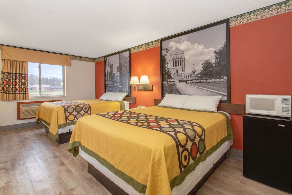Een hotelkamer met twee bedden, een magnetron, een kachel en een groot raam met gordijnen.