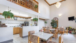 A spacious dining area with wooden chairs and tables, a kitchen in the background, and hanging plants. - Super 8 by Wyndham Bedford (Bedford)