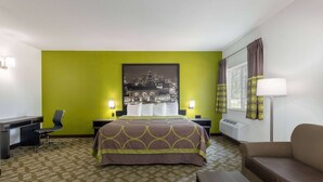 Habitación de hotel con cama, escritorio, silla, sofá y un amplio ventanal con cortinas.