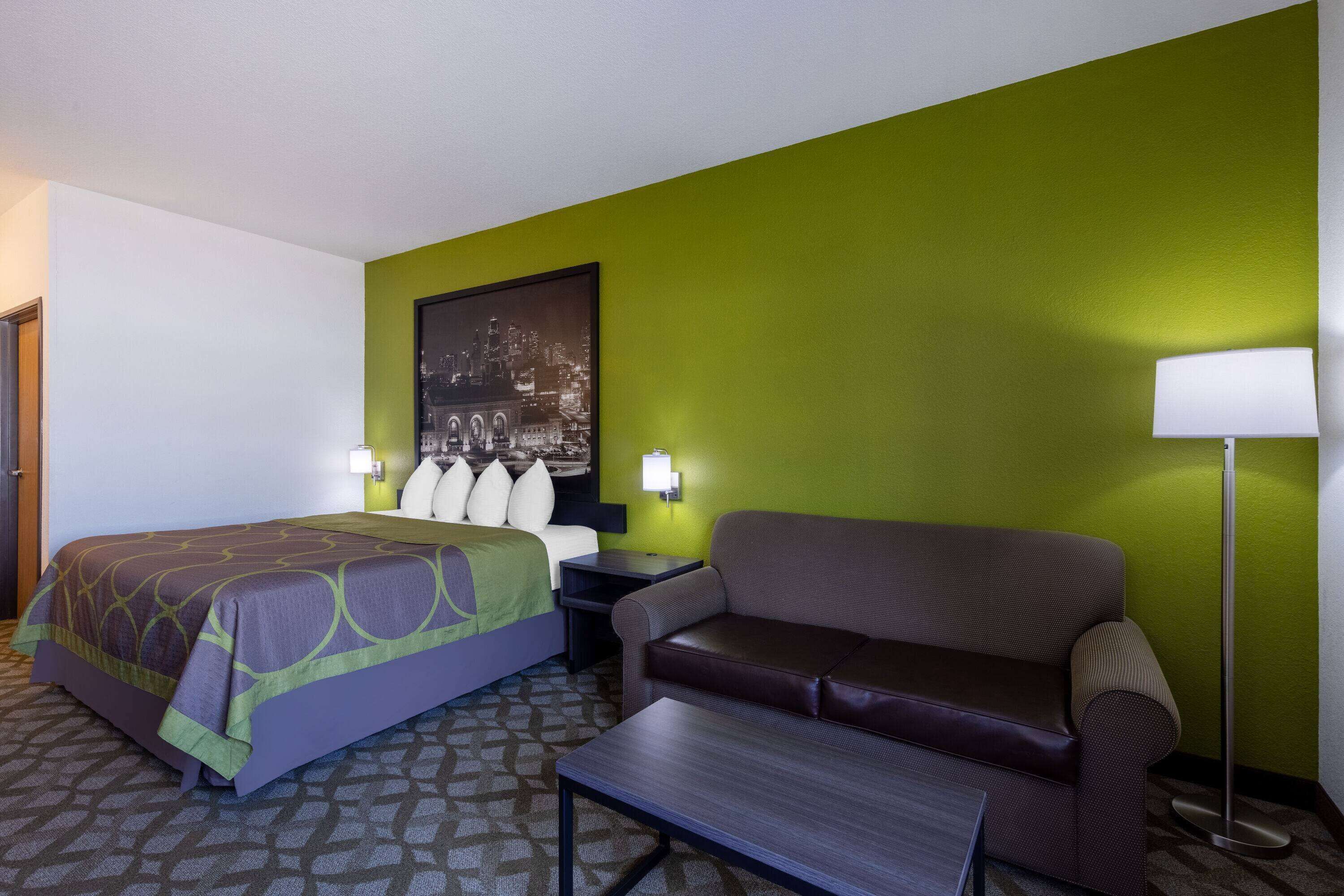 A hotel room with a bed, a sofa, a nightstand, a lamp, and a wall-mounted picture.