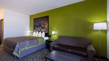 A hotel room with a bed, a sofa, a nightstand, a lamp, and a wall-mounted picture.