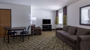 Habitación de hotel con sofá, televisor, mesa de comedor con sillas y alfombra estampada.