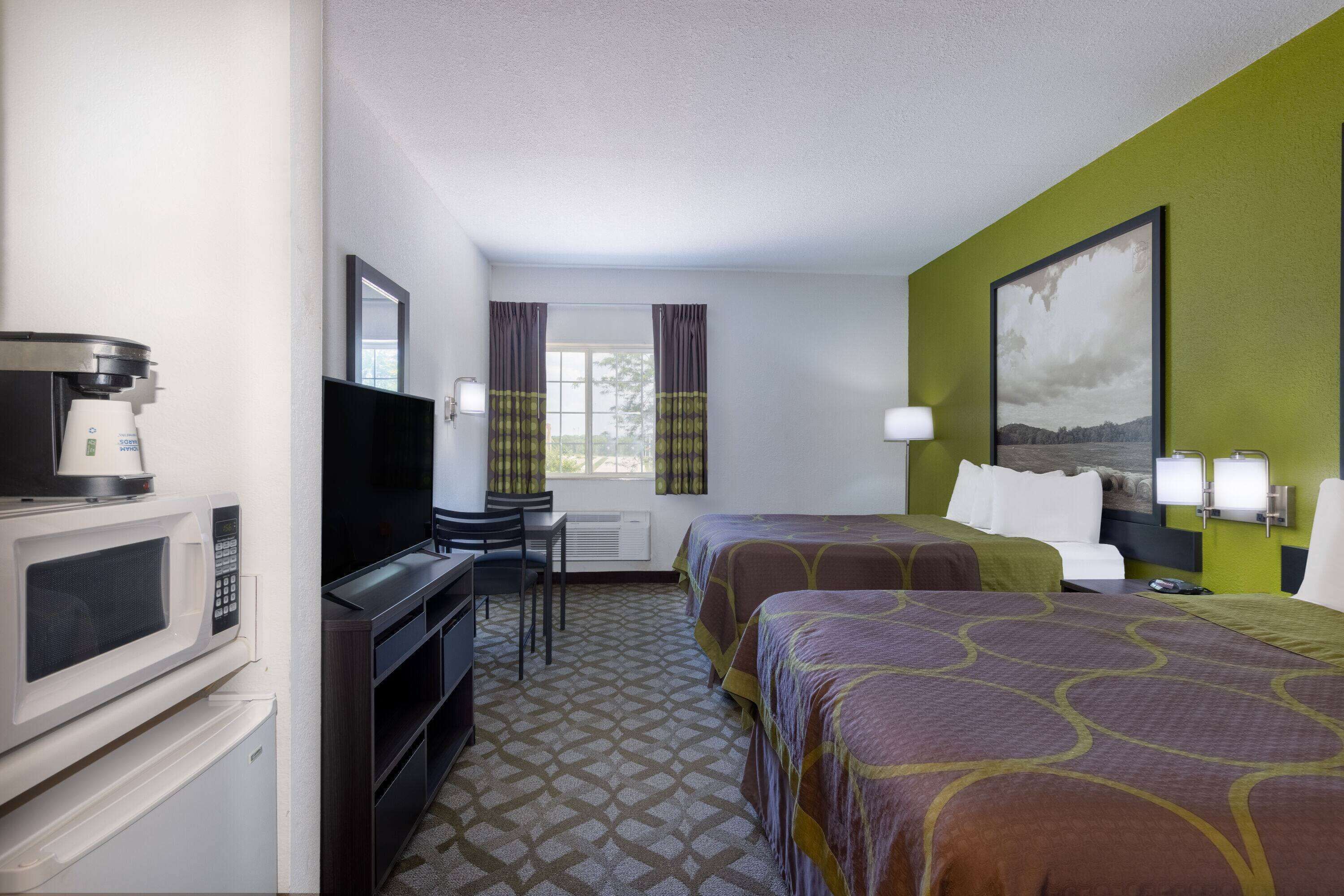 A hotel room with two beds, a desk with a chair, a television, a microwave, and a window with curtains.