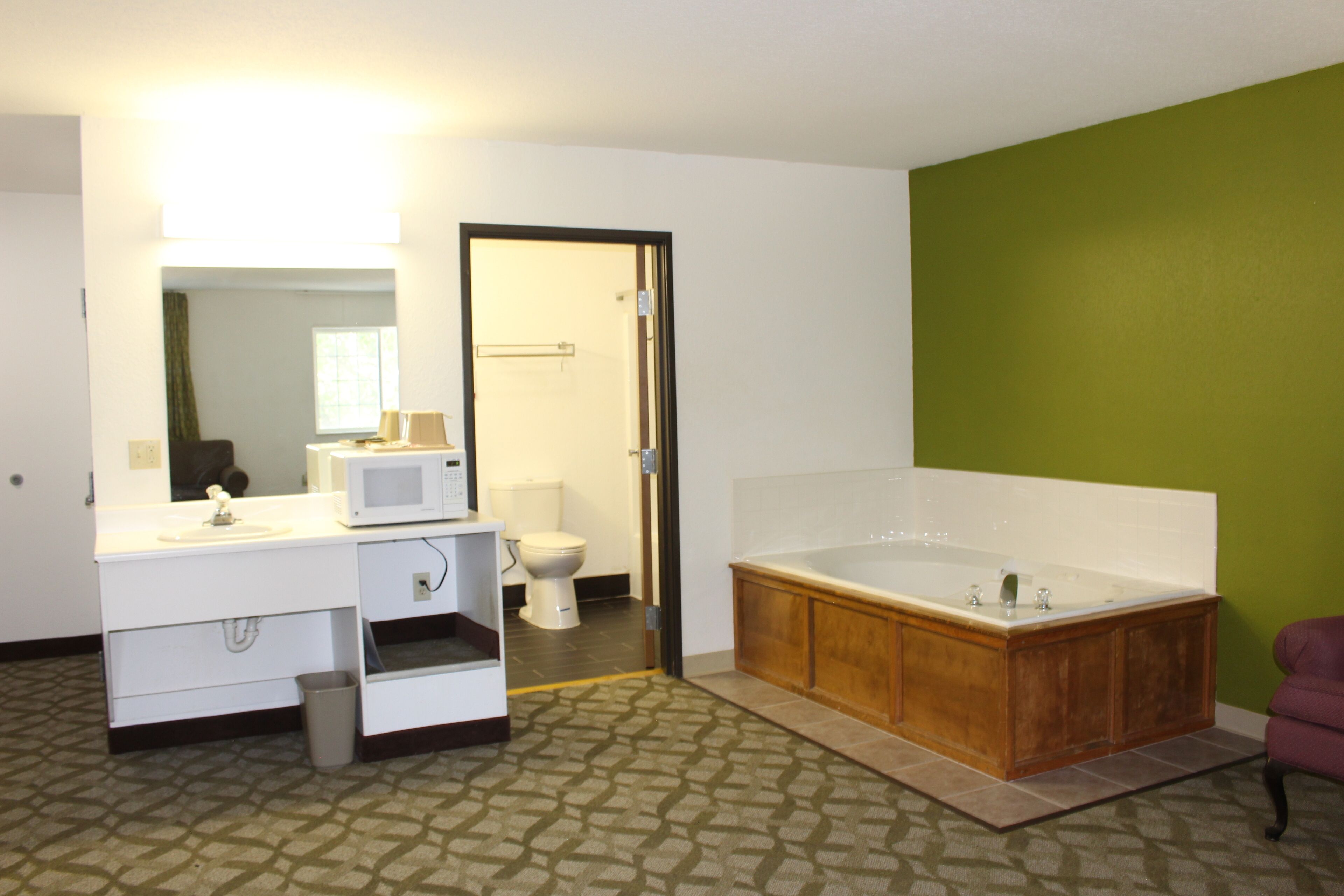 Une salle de bain avec un lavabo blanc, une baignoire en bois, un mur vert et un sol à motifs.