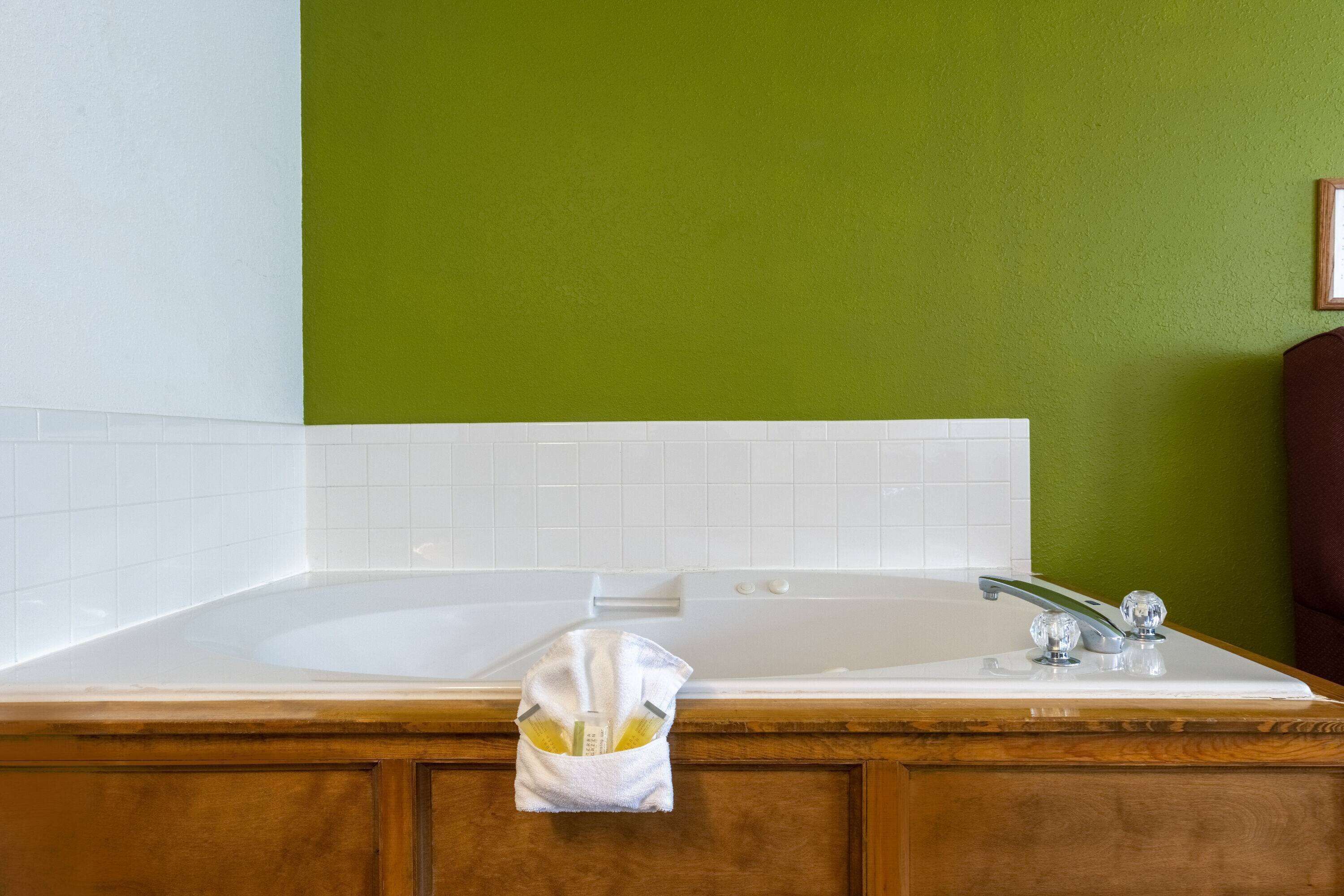 Un baño con una bañera blanca, paredes verdes y muebles de madera.