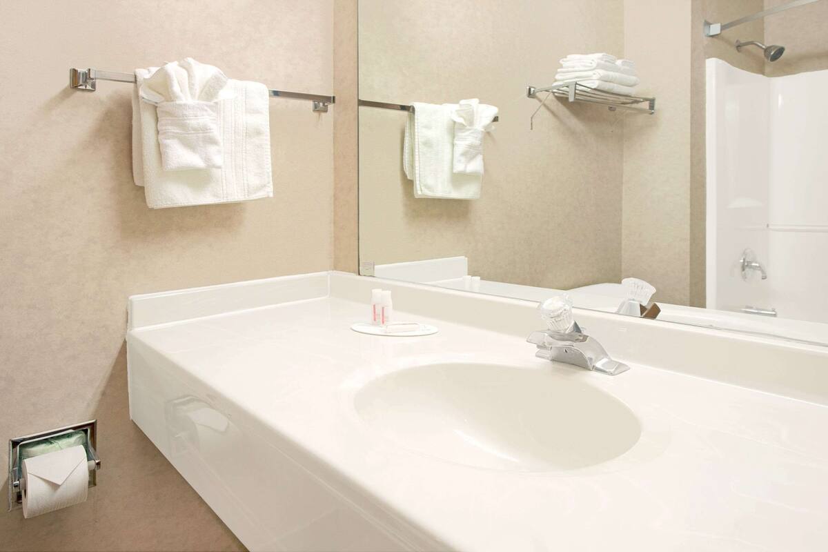 Une salle de bain moderne avec un grand lavabo blanc, un miroir et deux porte-serviettes sur lesquels sont soigneusement pliées des serviettes.