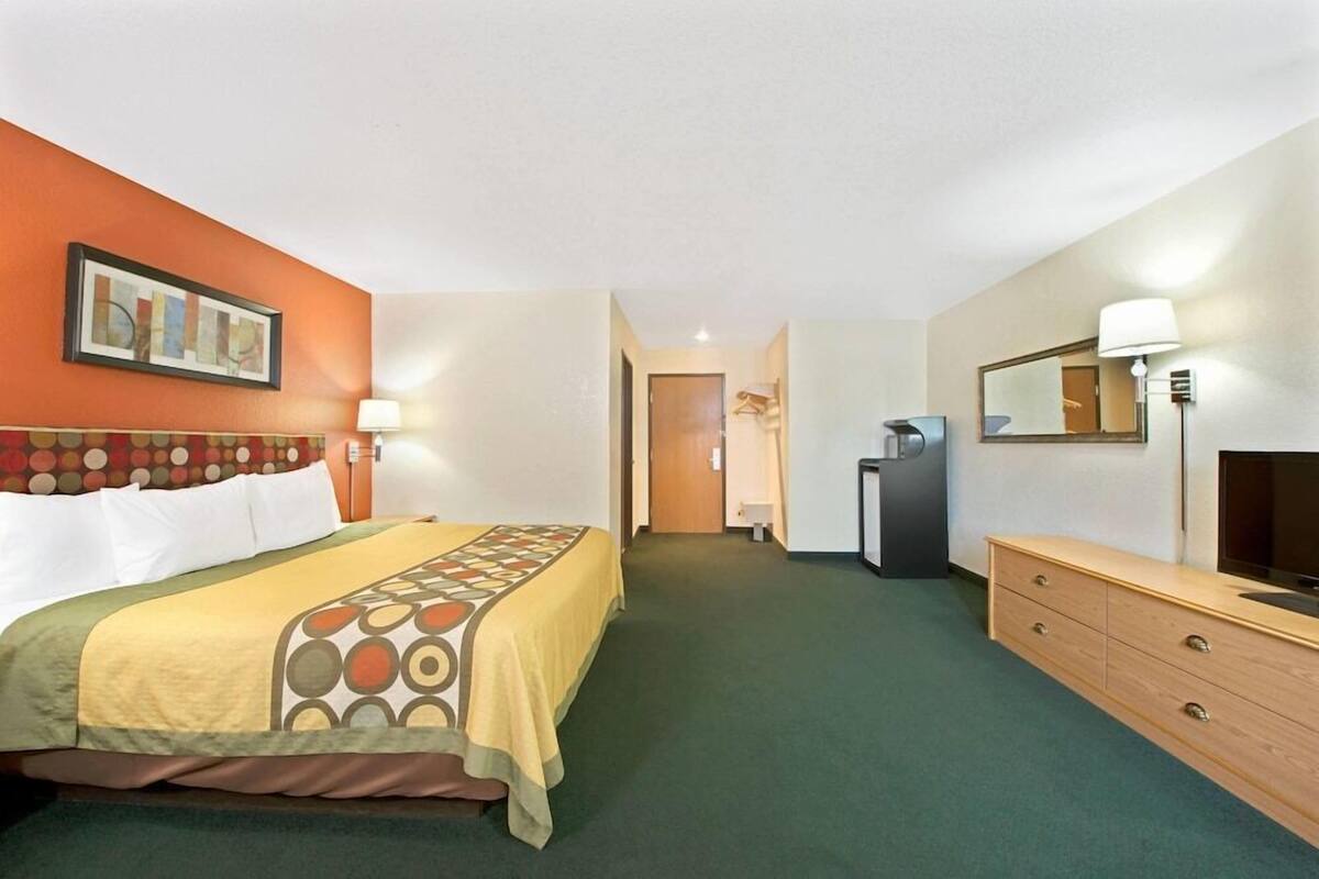 Une chambre d’hôtel comprenant un lit, une commode, une télévision et une porte donnant accès à une salle de bain.