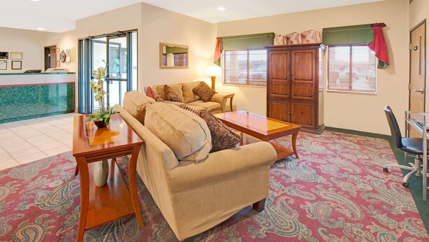 A living room with a sofa, coffee table, and a small table with a vase. There is a window with blinds and a door in the background. - Super 8 by Wyndham Bonne Terre (Bonne Terre)