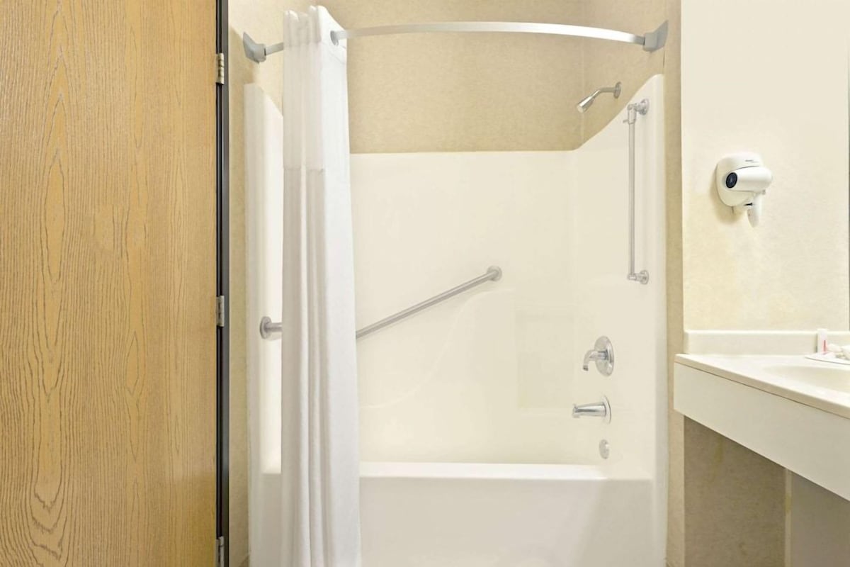 A bathroom with a shower, a handrail, a toilet, and a sink.