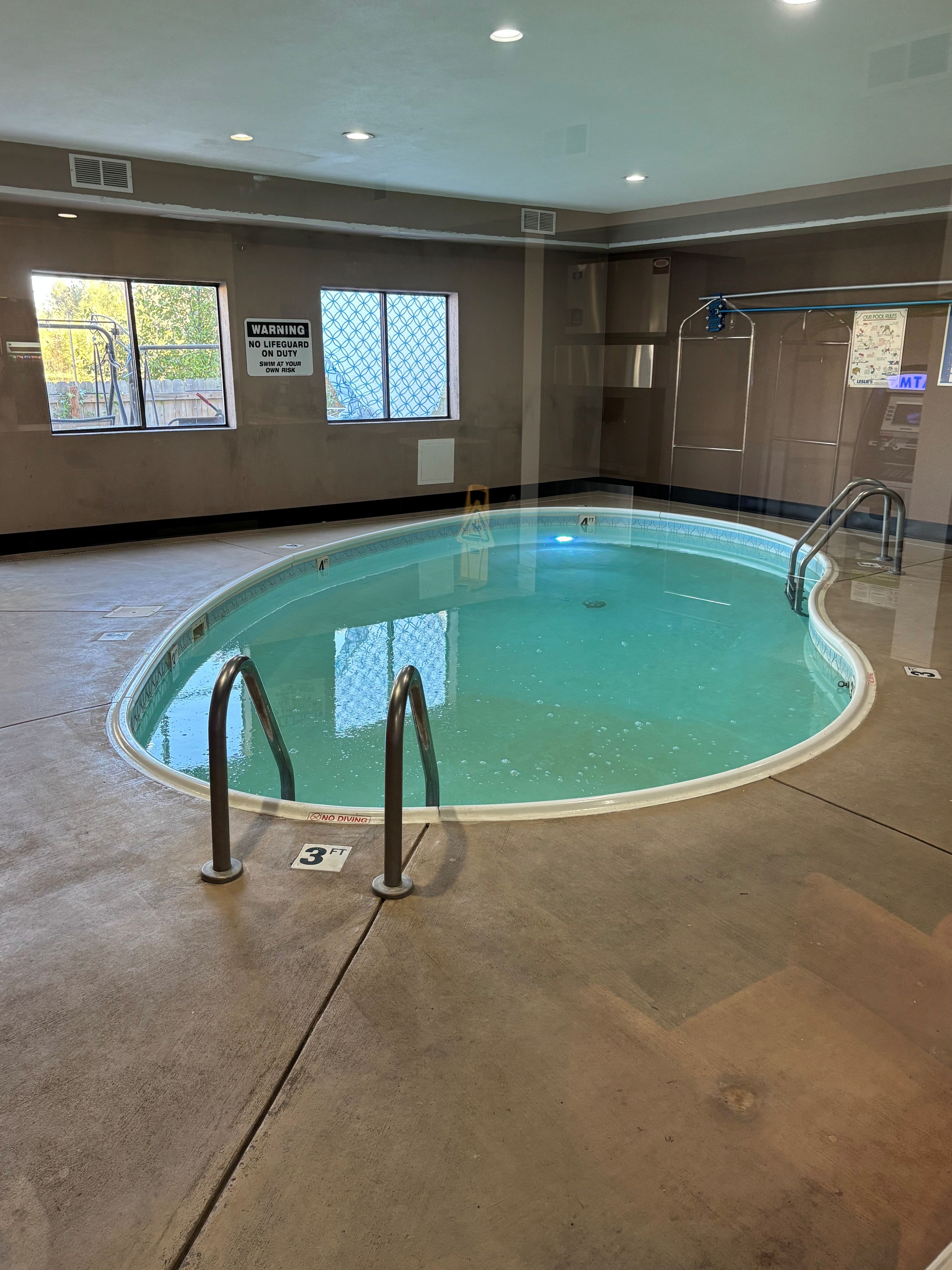 An indoor swimming pool with clear water, a lifeguard station, and a warning sign.