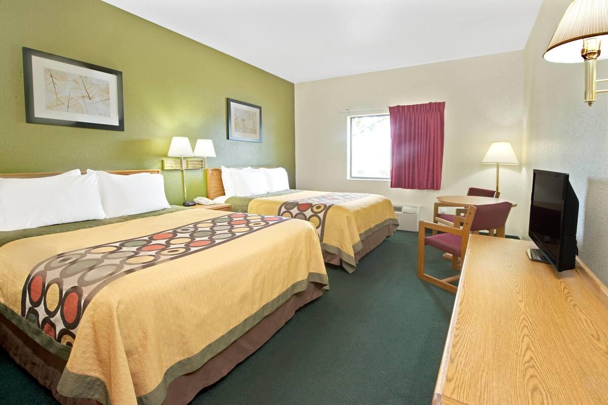 Une chambre d’hôtel avec deux lits, un bureau avec une télévision et une fenêtre avec un rideau rouge.