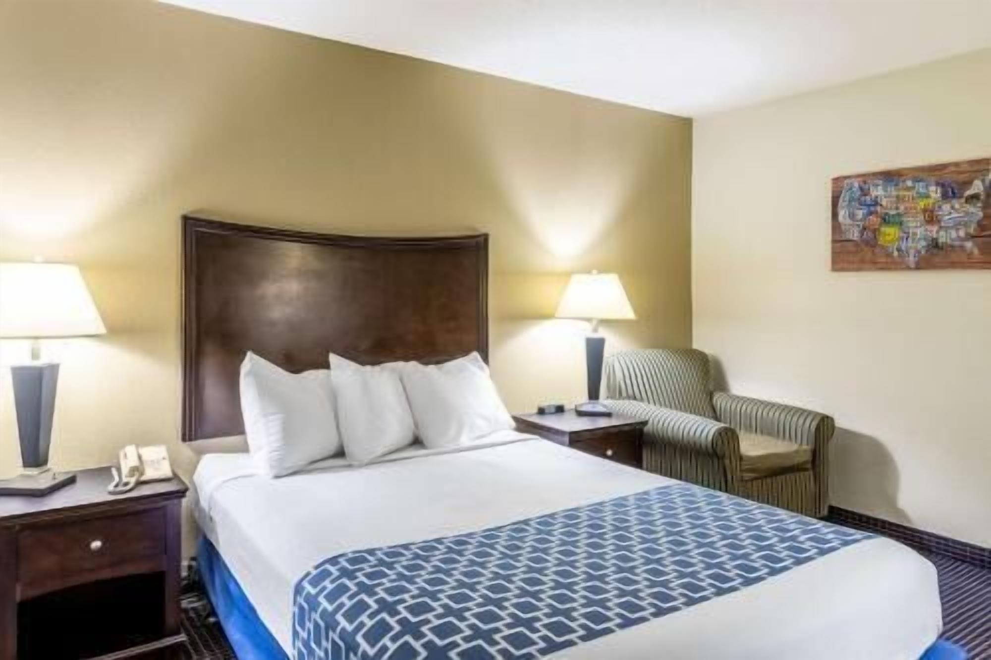 Une chambre d’hôtel comprenant un lit, deux tables de chevet, une chaise et un tableau accroché au mur.