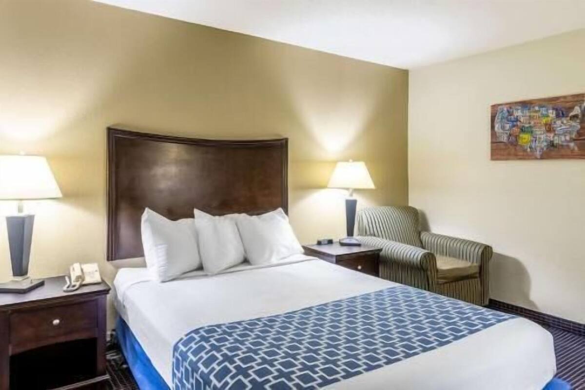 A hotel room with a bed, two bedside tables, a chair, and a wall-mounted painting.