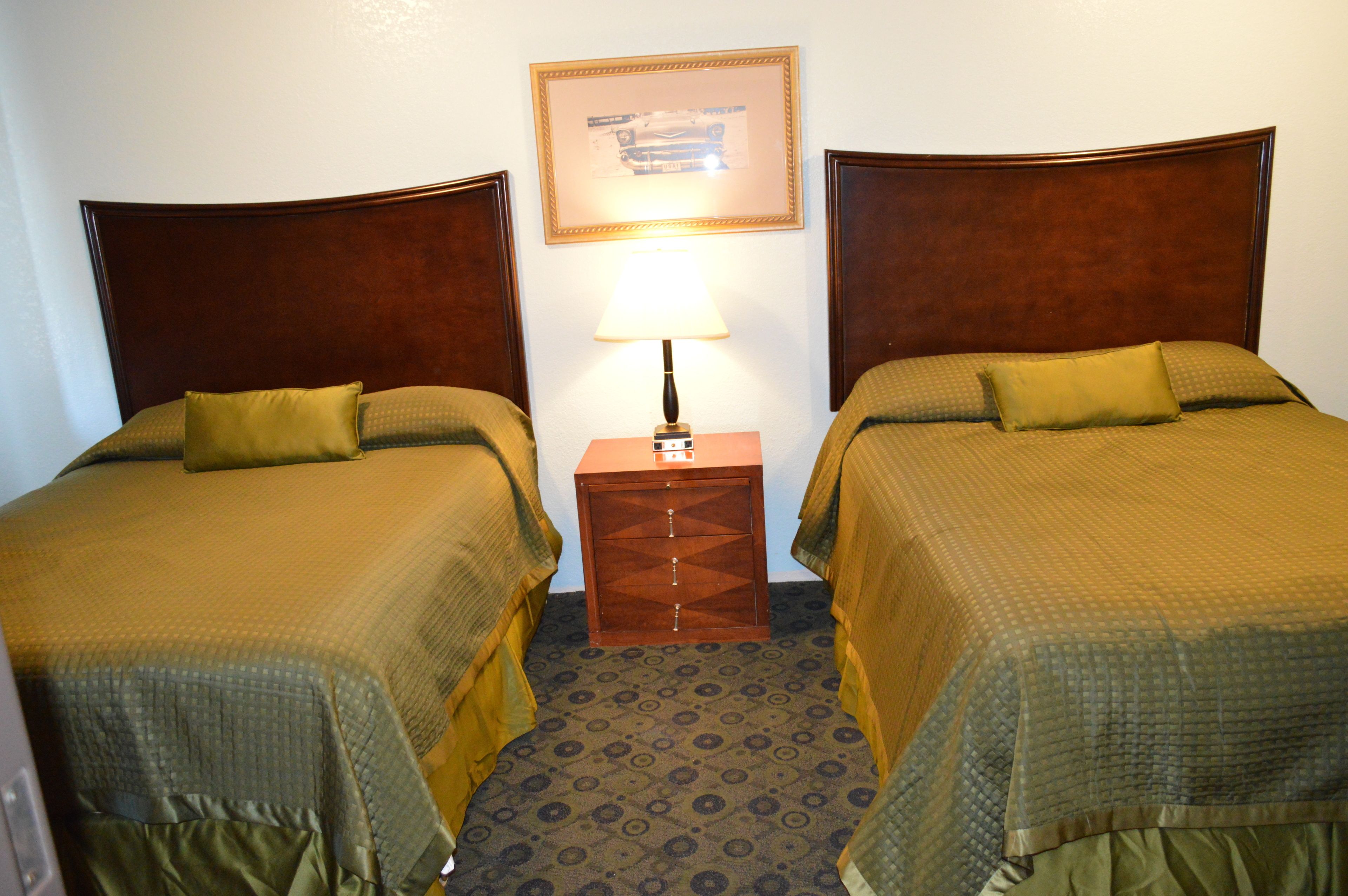 Una habitación de hotel con dos camas individuales, una mesita de noche con una lámpara y un cuadro enmarcado en la pared.