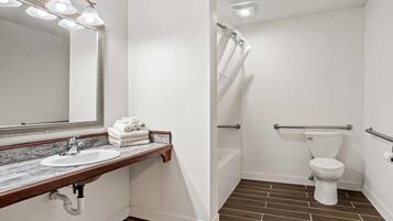 A bathroom with a white sink, mirror, and toilet. There are towels on the sink, a shower curtain, and a grab bar near the toilet.