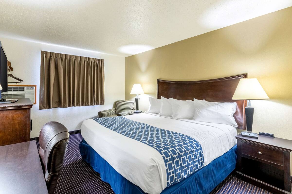 A hotel room with a large bed, two bedside lamps, a desk with a chair, and a television.