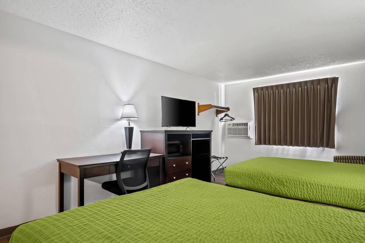A hotel room with two beds, a desk, a chair, a TV, a lamp, and a window with curtains.