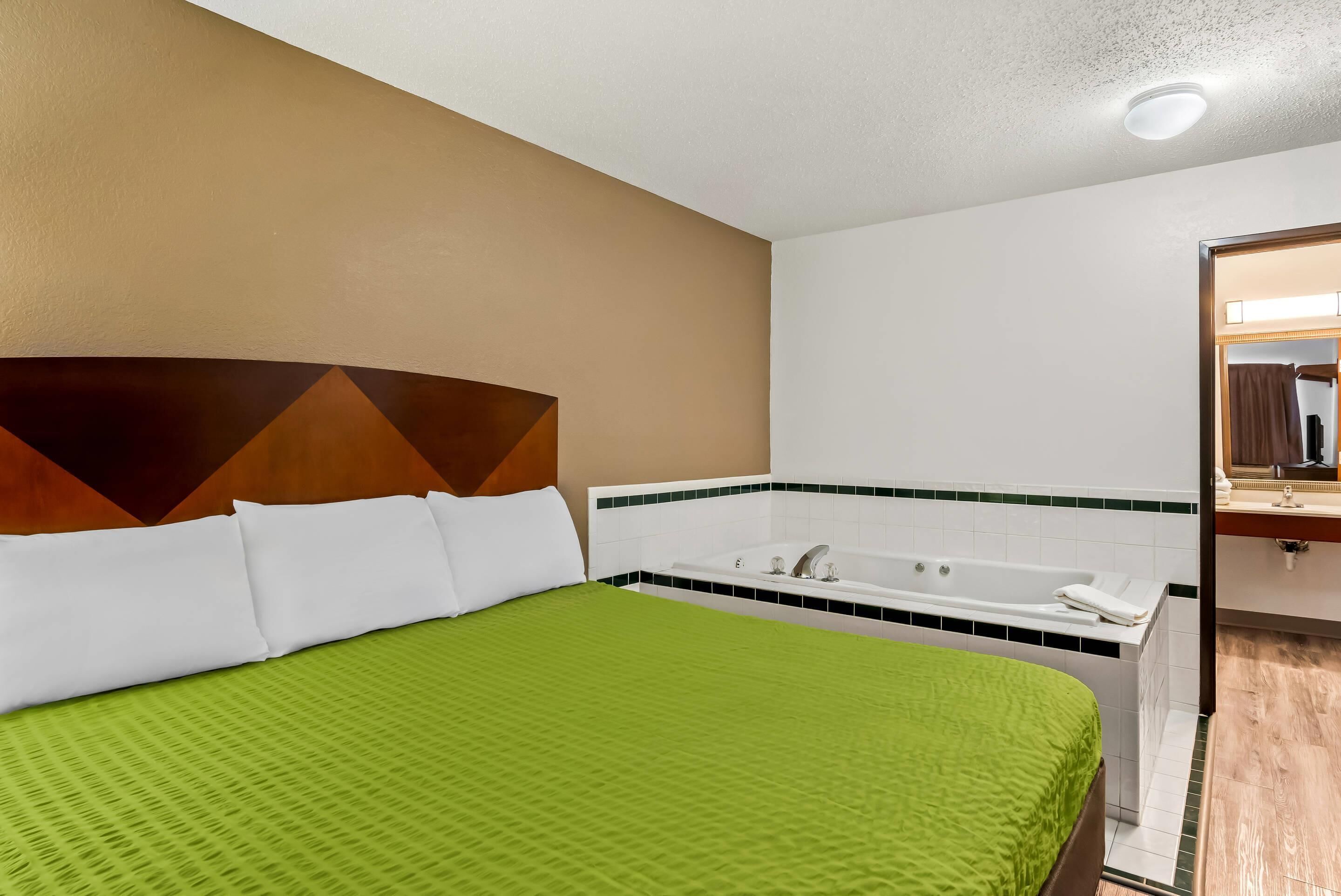 A hotel room with a bed, a bathtub, and a bathroom with a mirror and sink.