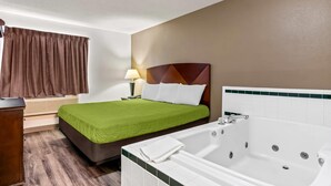 A hotel room with a bed, a large white bathtub, a wooden dresser, and a window with brown curtains. - Econo Lodge Inn & Suites Auburn (Auburn)