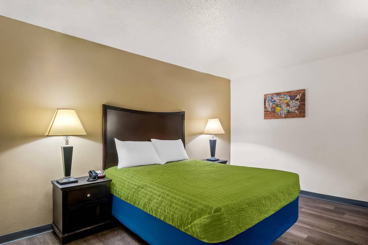 A hotel room with a bed, two bedside lamps, a nightstand, and a wall-mounted artwork.