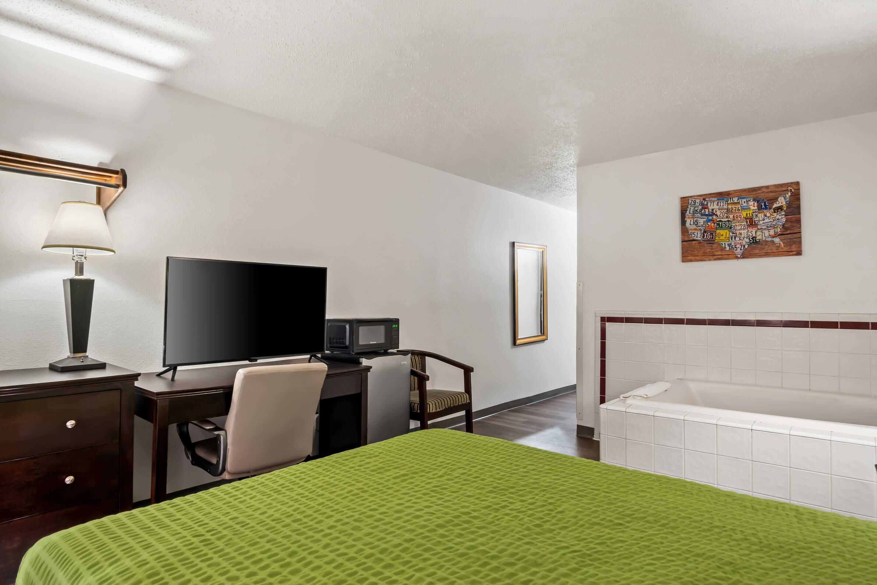 Habitación de hotel con cama, escritorio con computadora, televisión, microondas, silla, espejo y bañera.