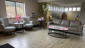 Una sala de estar moderna con un sofá gris, dos sillones, una mesa de centro y un ventanal con vistas a árboles.