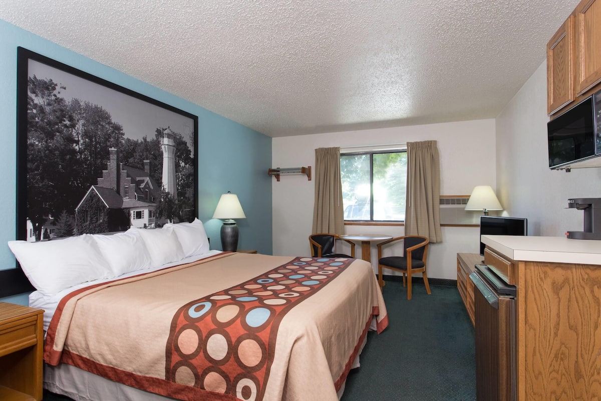 A hotel room with a bed, a desk, a chair, a TV, and a window with curtains.