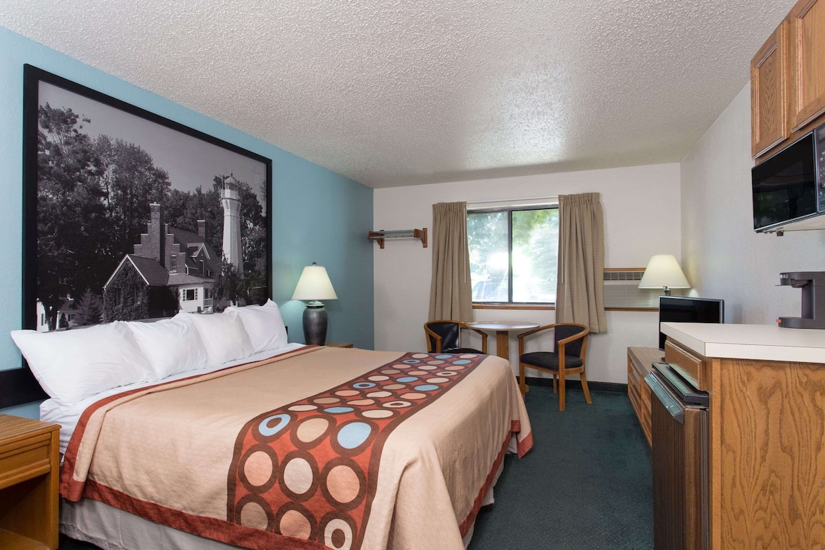 A hotel room with a bed, a desk, a chair, a TV, and a window with curtains.