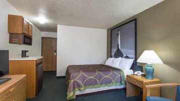 A hotel room with a bed, a desk with a computer, a microwave, a lamp, and a chair.