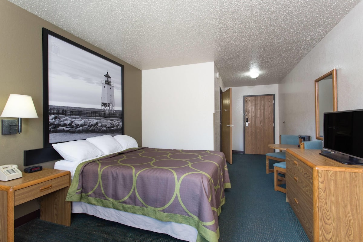 A hotel room with a bed, a desk, a chair, a television, and a large framed picture on the wall.
