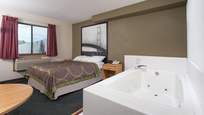 Habitación de hotel con cama, un ventanal con cortinas, unidad de aire acondicionado, mesita de noche con teléfono y una bañera.