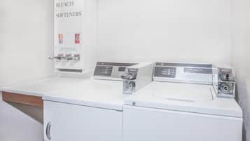 A laundry area with a soap and bleach dispenser, two washing machines, and a cabinet.