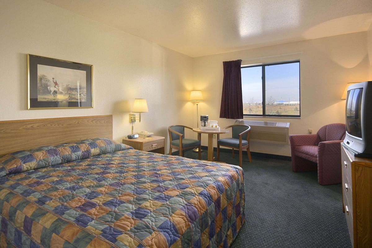 A hotel room with a large bed, a desk with a chair, a television, and a window with curtains.