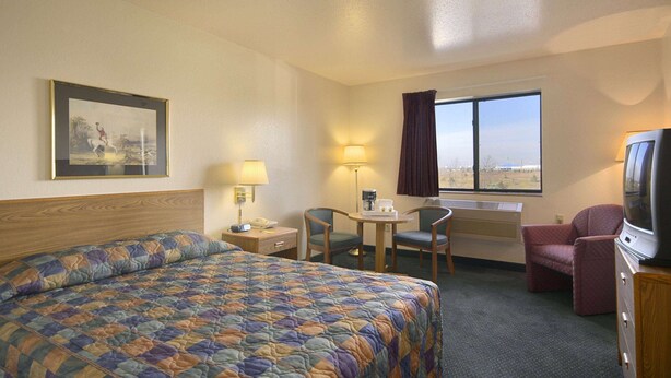 A hotel room with a large bed, a desk with a chair, a television, and a window with curtains.