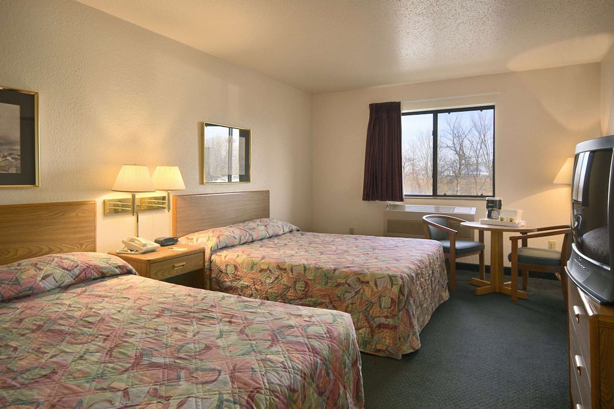 A hotel room with two beds, a desk, a chair, a television, and a window with curtains.