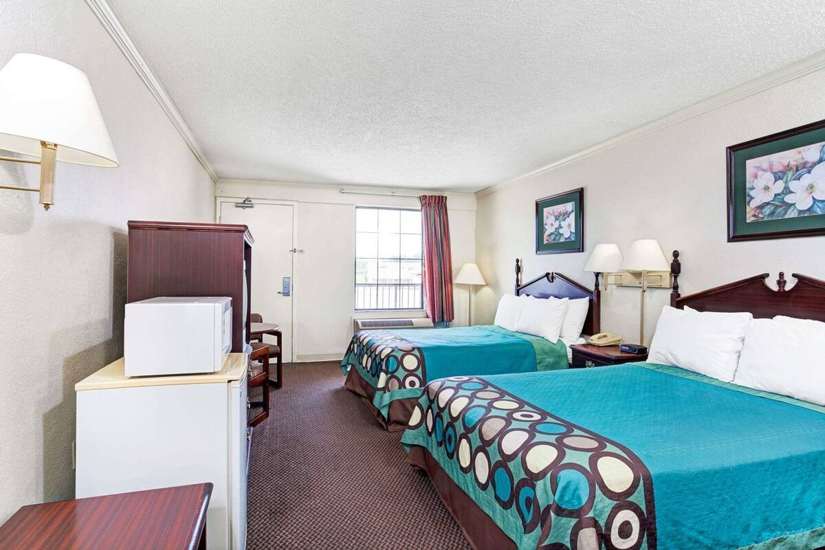 A hotel room with two beds, a desk, a chair, a television, and a window with curtains.