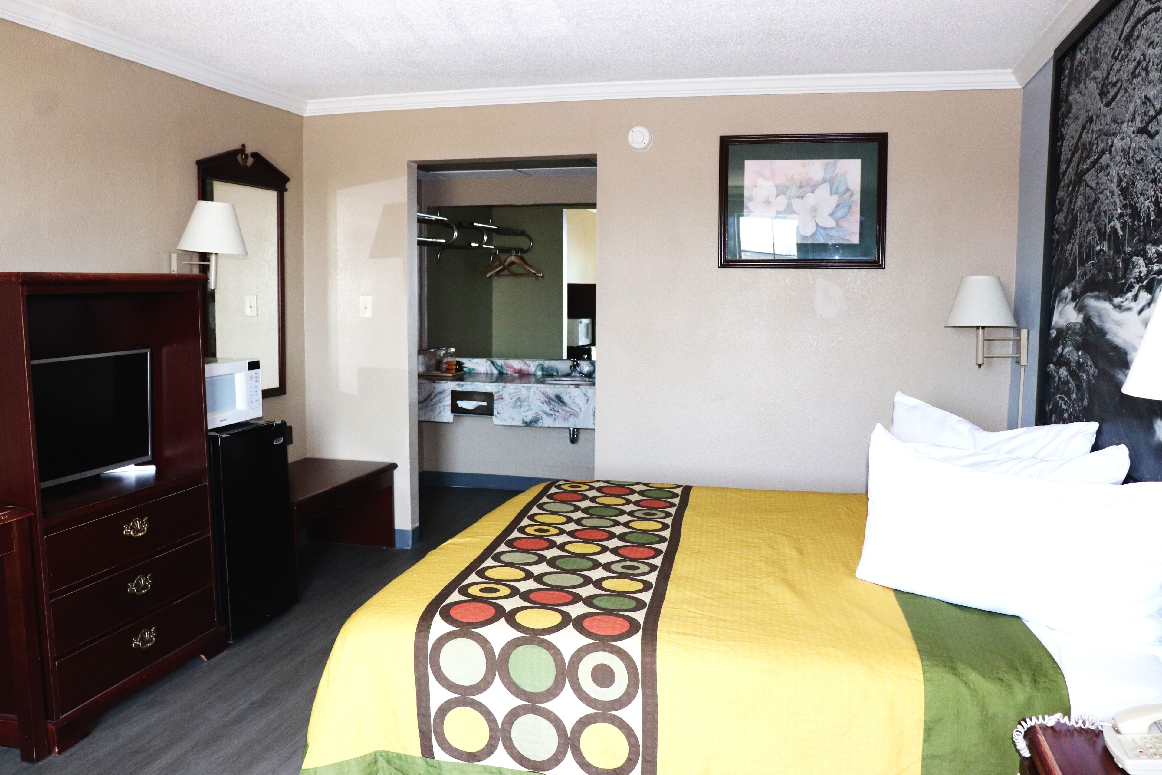 A hotel room with a bed, a TV, a dresser, a mirror, and a bathroom visible through an open door.