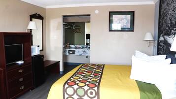 Quarto de hotel com cama, televisão, penteadeira, espelho e banheiro visível por uma porta aberta.