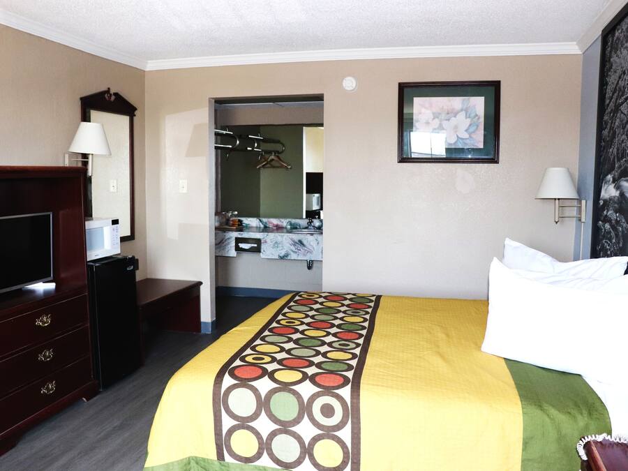 Quarto de hotel com cama, televisão, penteadeira, espelho e banheiro visível por uma porta aberta.