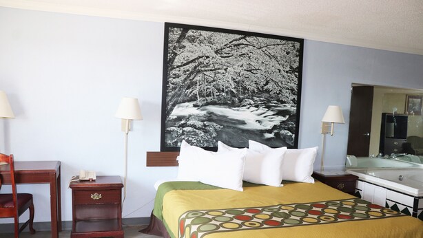 A hotel room with a bed, a desk, a chair, a nightstand, a lamp, and a large painting of a waterfall. - Super 8 by Wyndham Clarksville East (Clarksville)