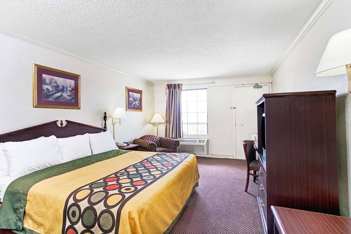 Habitación de hotel con cama, escritorio, silla, televisor y dos cuadros en la pared.