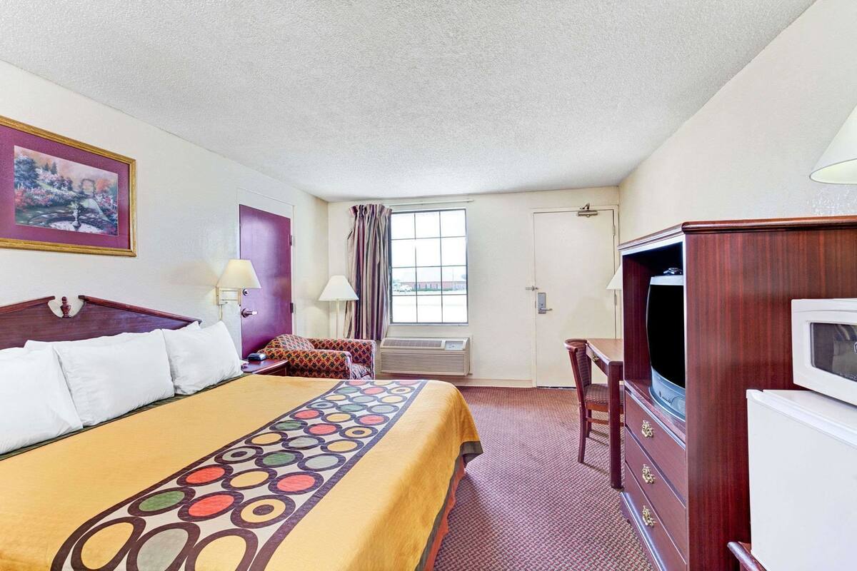 A hotel room with a bed, a desk, a television, and a window with curtains.