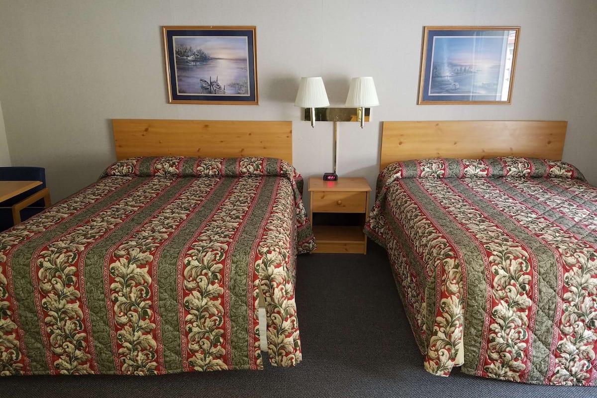 A hotel room with two beds, each with a patterned bedspread, a nightstand with a lamp, and two framed pictures on the wall.