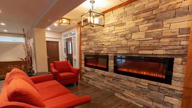 A modern living room with a stone fireplace, red upholstered chairs, and a round wooden table. - The Kanata by BCMInns Invermere (Invermere)