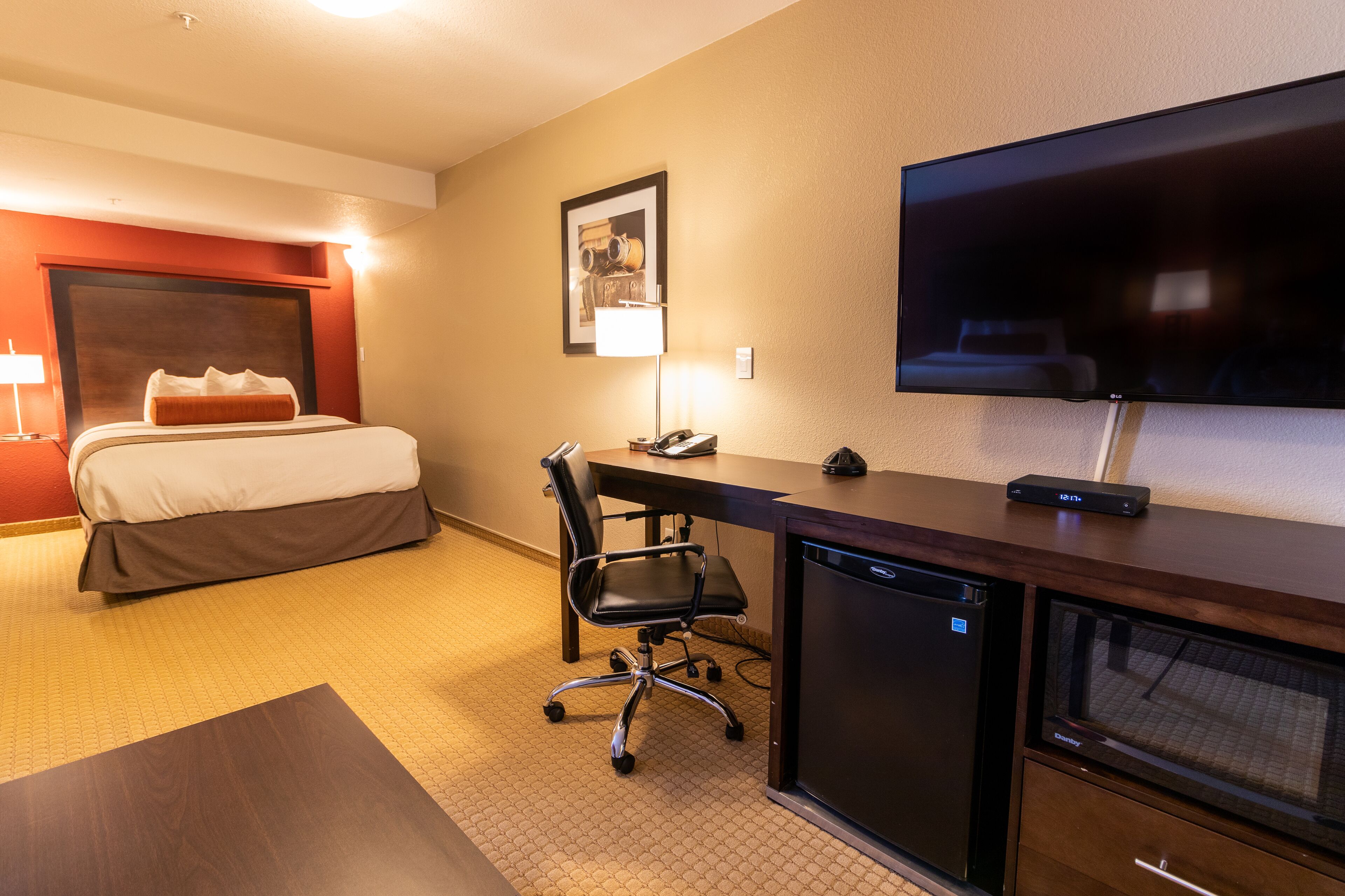 Une chambre d’hôtel équipée d’un lit, d’un bureau, d’une chaise, d’une télévision et d’un petit réfrigérateur.