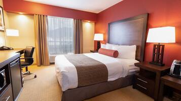 A hotel room with a large bed, two bedside tables with lamps, a desk with a chair, and a window with curtains.