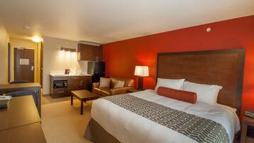 A hotel room with a large bed, a desk, a chair, a sofa, a microwave, a refrigerator, and a lamp.
